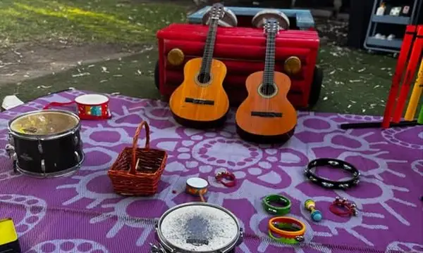 An outdoor music circle on a picnic rug: two small guitars, a hand drum, tambourines and percussion instruments, all recently sourced from Reverse Garbage.
