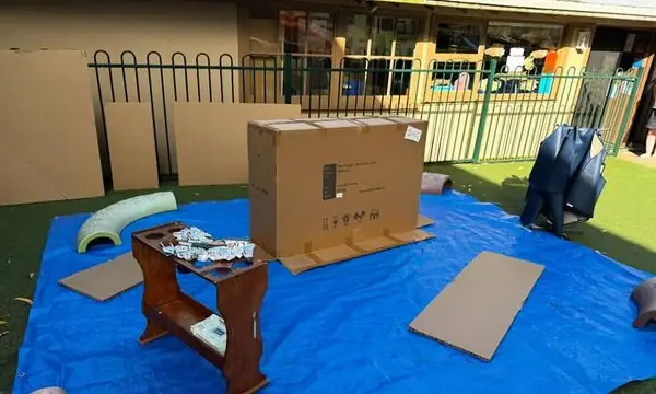 A Reggio-inspired outdoor painting invitation with large cardboard boxes as blank canvases, set up on a tarp in the playground for whole-body, large-scale mark-making.